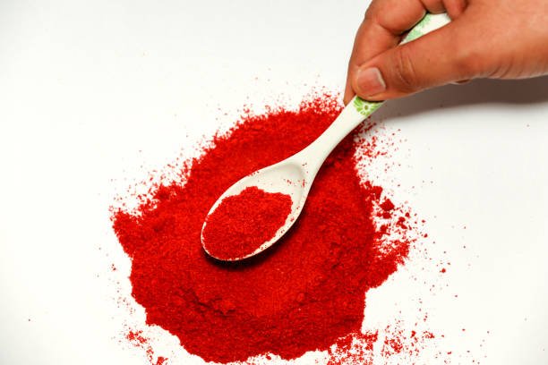 Human hand picking up red chili power with spoon isolated on white background.